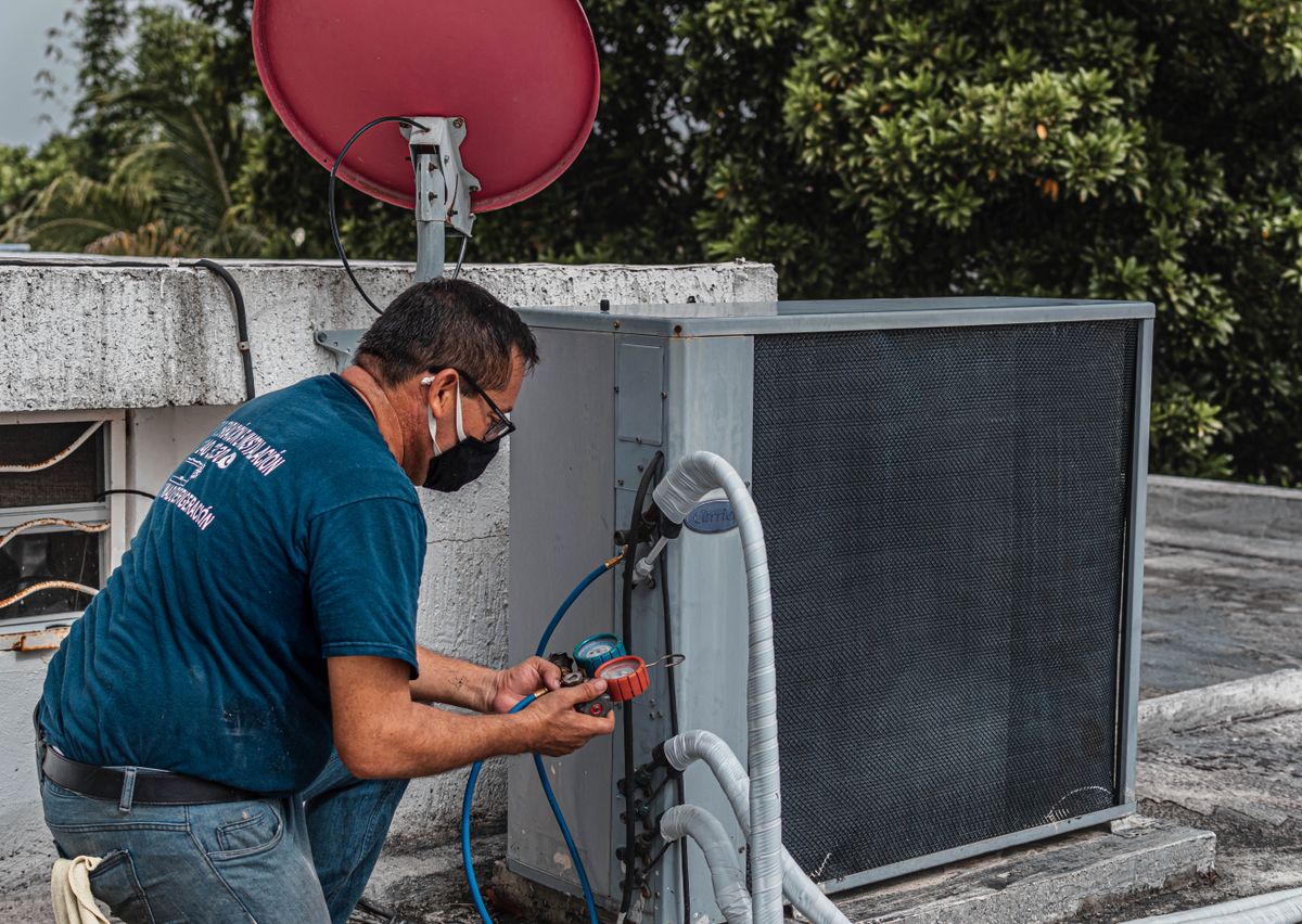 Technician checking pressure gauges beside an outdoor air conditioning unit on a roof.