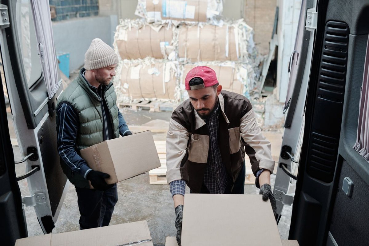 Two workers loading cardboard boxes into the back of a moving van.