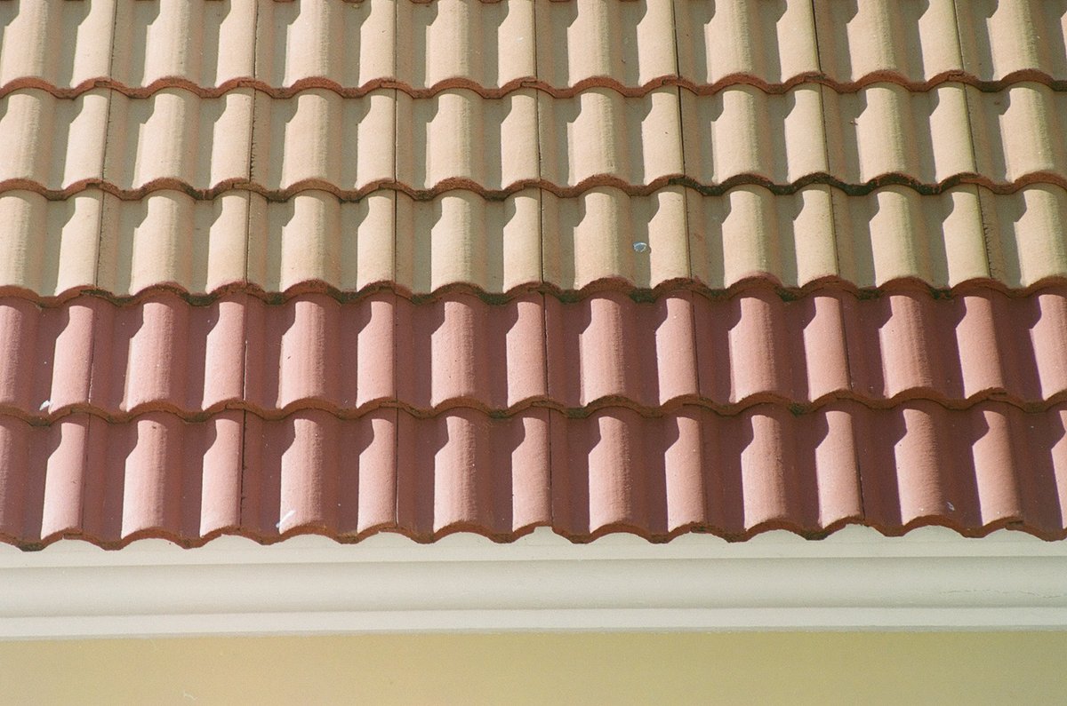 Sunlit tan and reddish interlocking roof tiles above a white gutter.