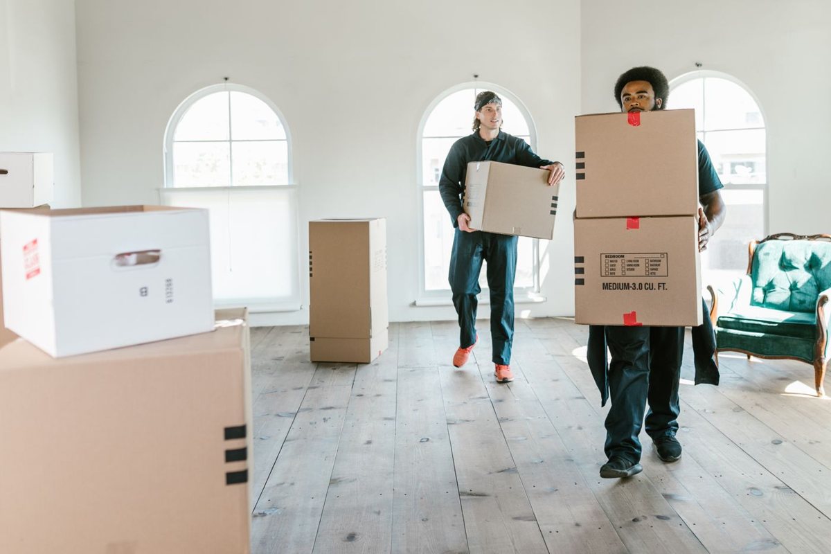 Two professional movers carrying cardboard boxes inside a home.